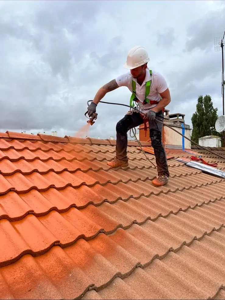 Couvreur encordé et casqué progressant sur un versant en tuiles