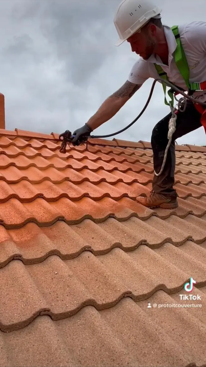 Couvreur encordé au travail sur un versant en tuiles