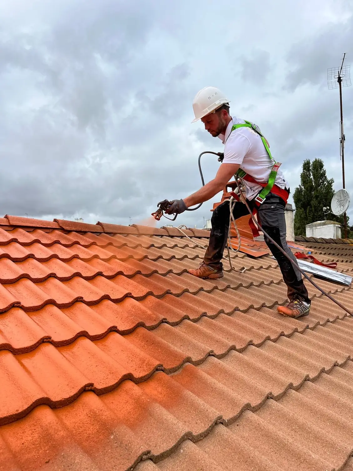 Couvreur casqué au pulvérisateur sur un versant en tuiles