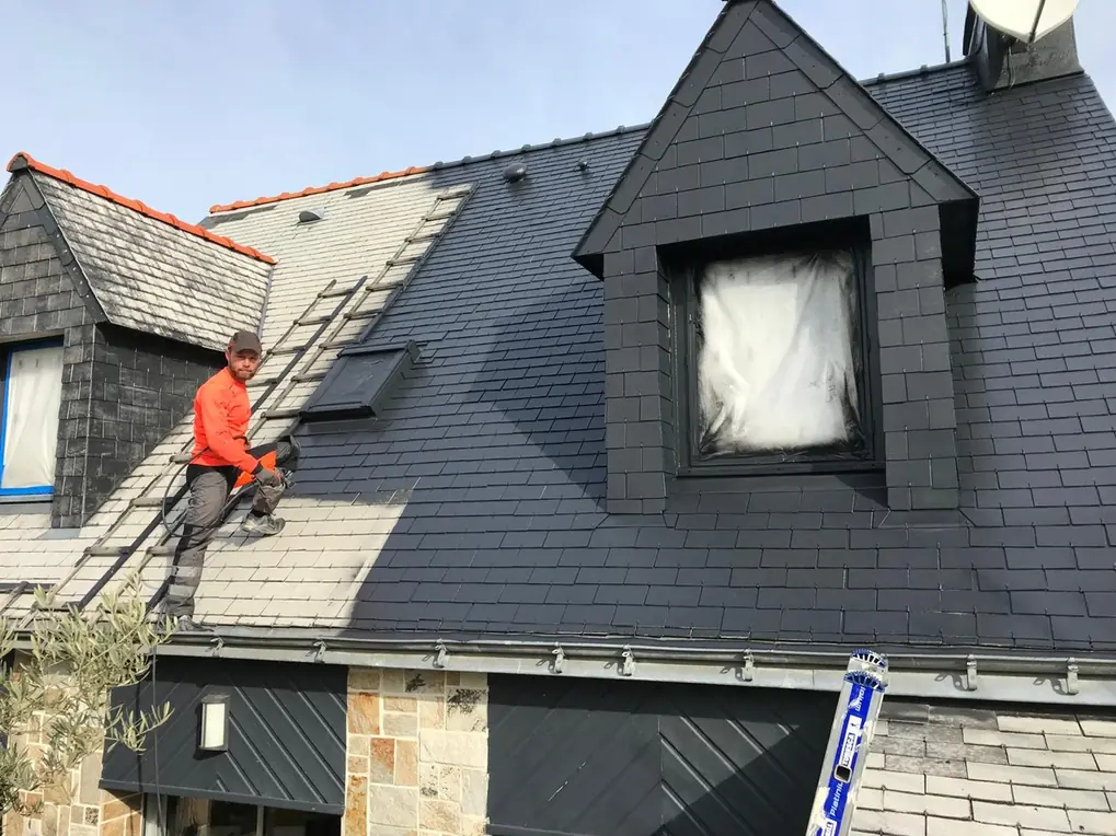 Maison en ardoise avec lucarne, couvreur en veste orange sur le versant